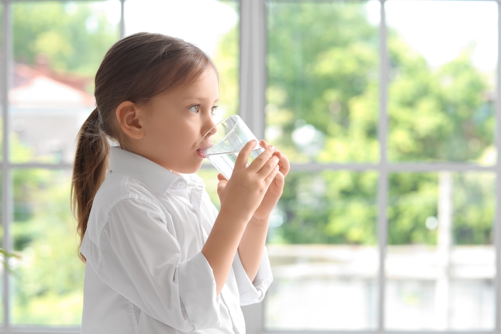 A young girls drinks water from a glass.