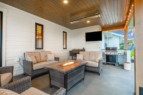 A backyard patio with seating, a fire table, and a TV.