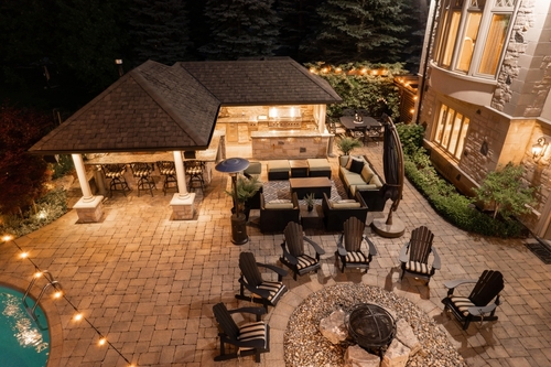 A paved outdoor space with a full outdoor kitchen, fire ring, and seating areas.