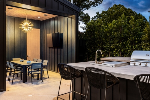 An outdoor kitchen with a grill and sink and a covered outdoor dining area with a TV.