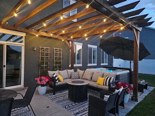A backyard patio with a pergola, string lights, and outdoor furniture.
