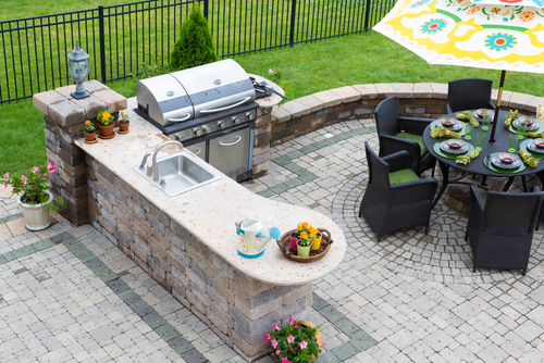 An outdoor kitchen with a sink, grill, and dining area.