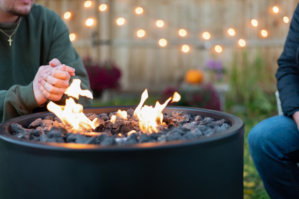 Two people gather around a smokeless fire pit in a backyard.
